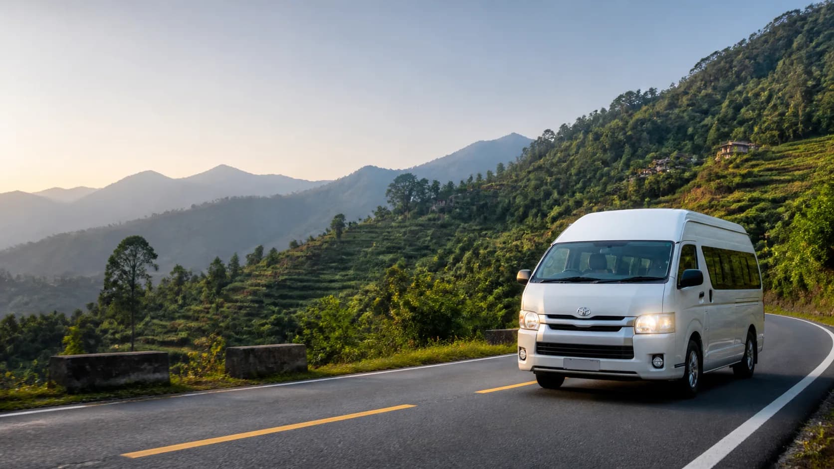 A comfortable white minibus traveling through Nepal's green mid-hills